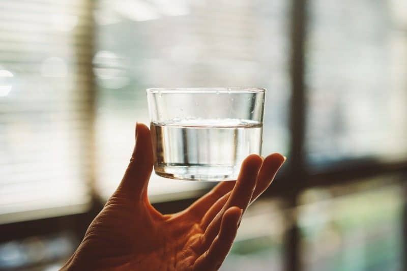 Eine Hand hält ein Glas mit klarem Wasser, das für die Transparenz steht, die rückblickende Sitzungen fördert.