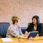Dos mujeres en una mesa negociando o conversando lo que podría ser una contratación o discusión de aumento salarial