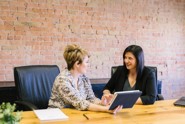 Dos mujeres en una mesa negociando o conversando lo que podría ser una contratación o discusión de aumento salarial