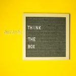 Pared amarilla con letrero vintage que dice "think out of the box"