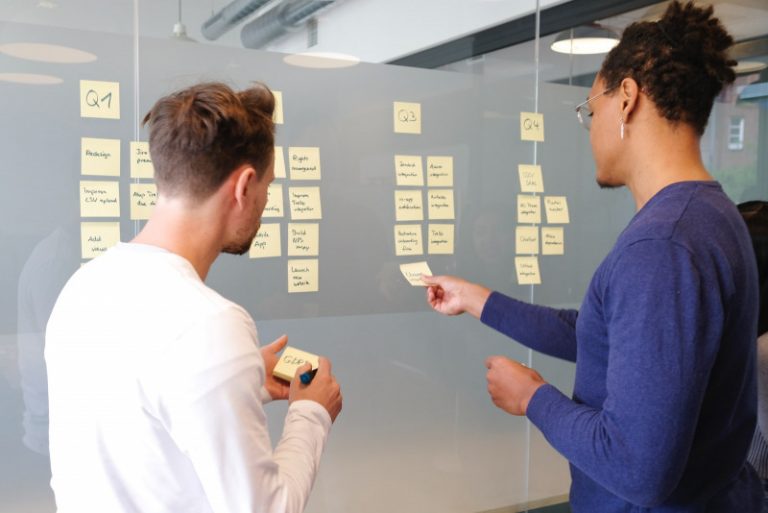Two people talking in front of a kanban board.
