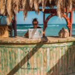 woman sitting on tiki bar facing silver laptop