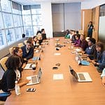people sitting beside rectangular brown table with laptops
